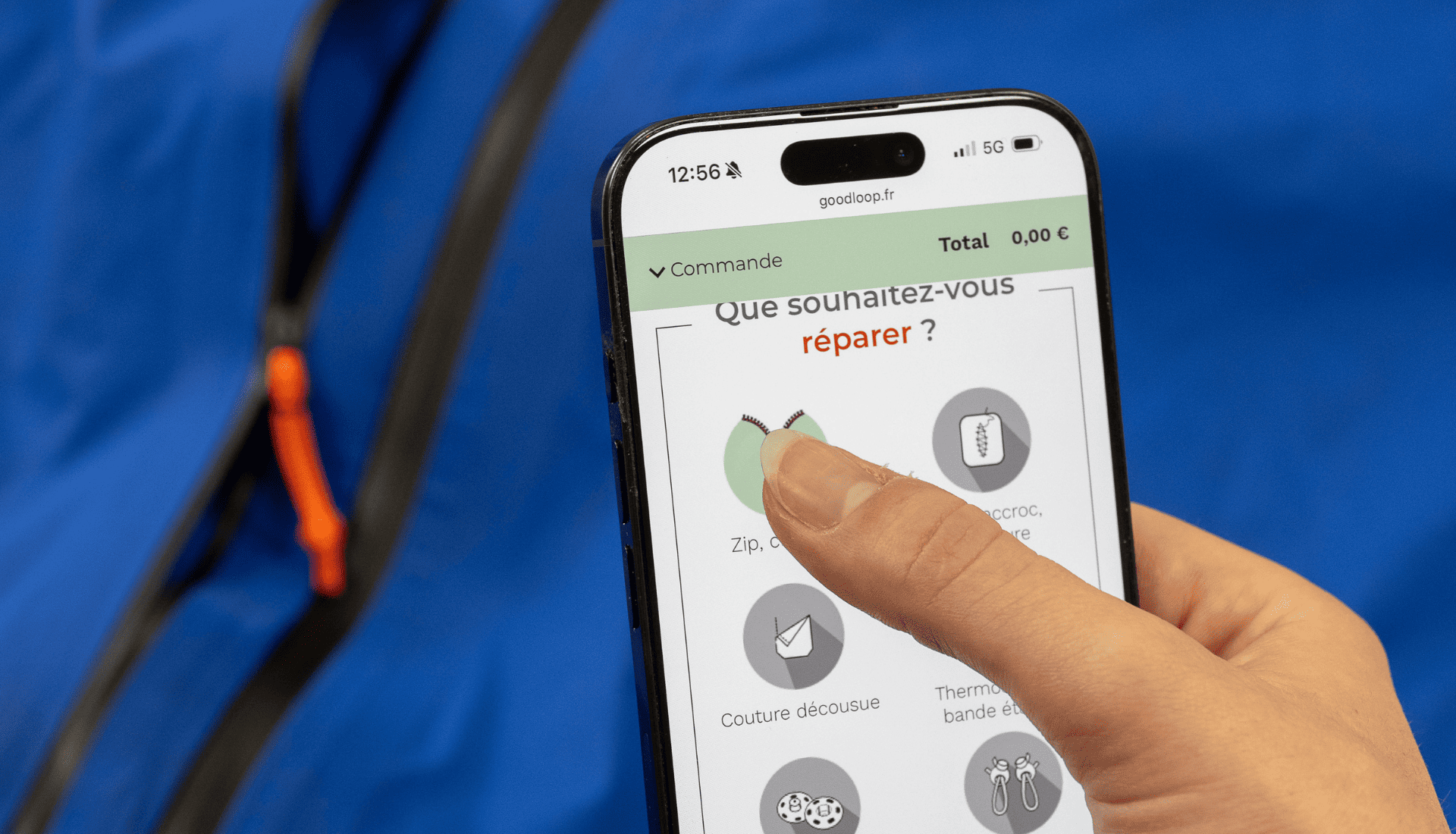Une personne commande une réparation sur le formulaire Goodloop pour un zip cassé, avec une veste bleue en arrière-plan.<br />
