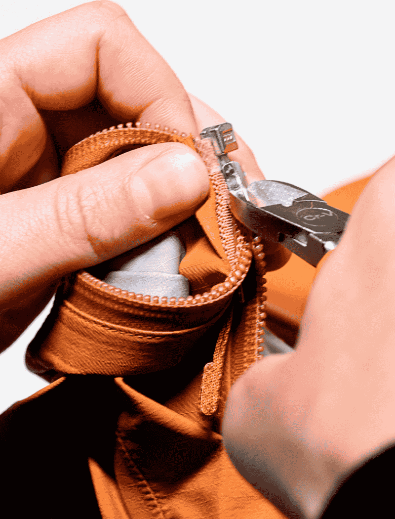 Réparation du curseur d’une fermeture éclair sur une veste technique Gore-Tex à l’aide d’une pince dans l’atelier Goodloop.